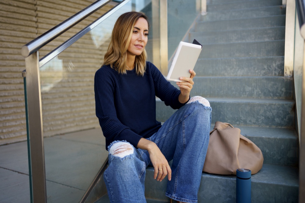 Middle-aged woman reading with her e-book on a coffee break near her office. Caucasian female wearing casual clothes.. Middle-aged woman reading with her e-book on a coffee break near her office.