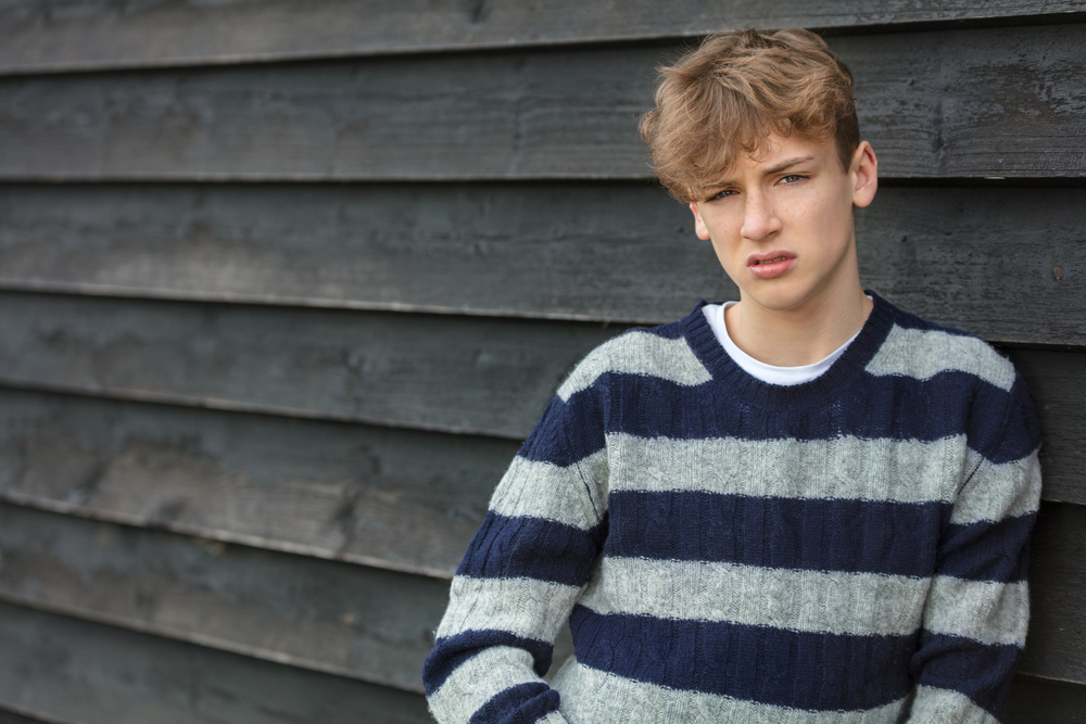 Serious male boy teenager young adult outside leaning on a wall wearing a striped jumper