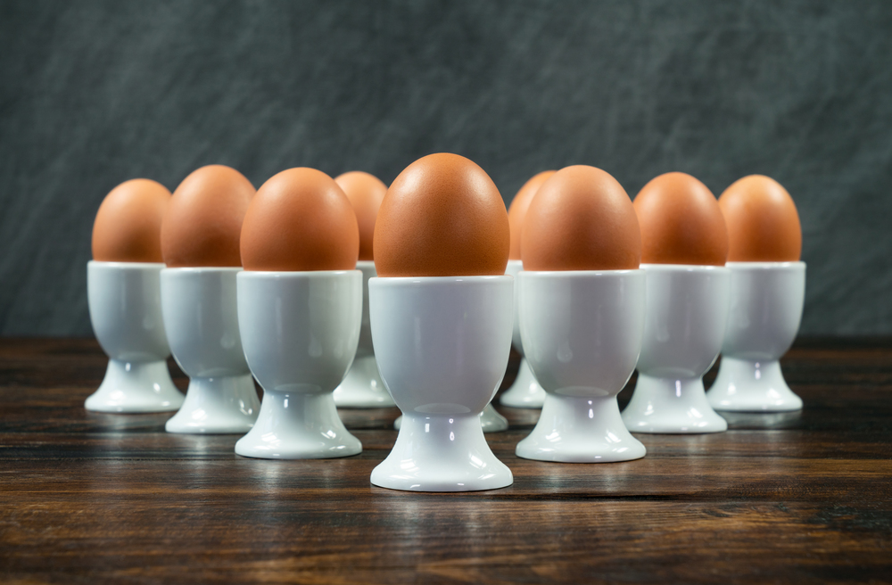 Ten boiled eggs in white egg cups on a wooden table in a triangle arrangement