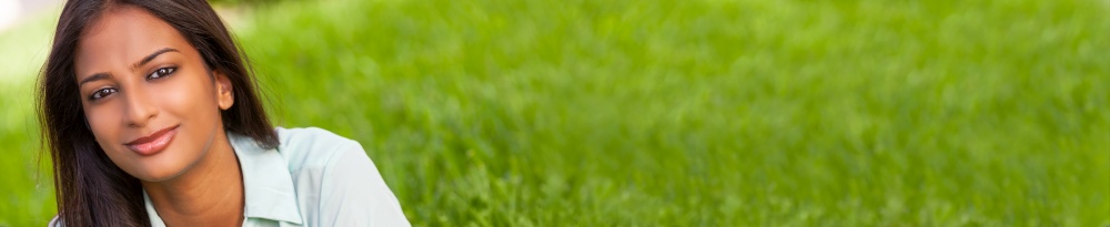 Panoramic outdoor portrait of a beautiful Indian Asian young woman or girl outside happy smiling laying down on grass panorama web banner header