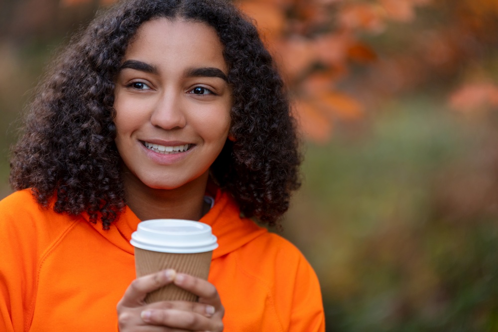 Beautiful happy mixed race African American girl teenager female young woman wearing an orange hoodie smiling drinking take out coffee outside during autumn or fall