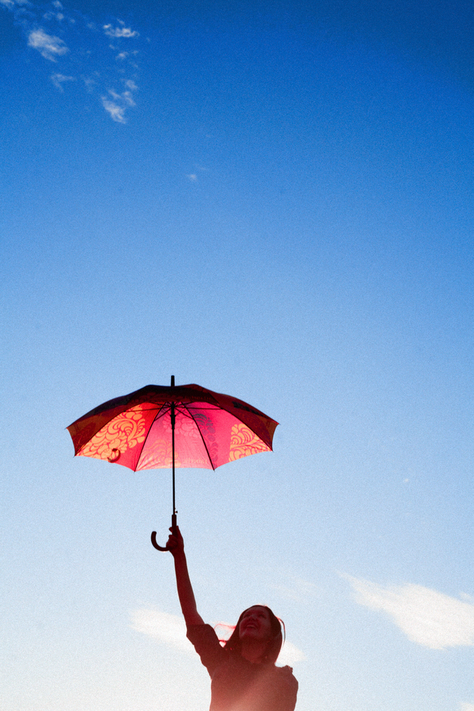 Beautiful young woman holding umbrella over clear sky. Freedom relax. Clear sky with gradient. Vintage looking image, backlit.