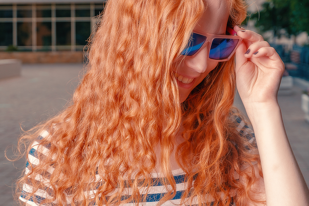 Ginger haired girl touching funny sunglasses and looking away and down. Ginger haired girl in funny sunglasses looking away and down
