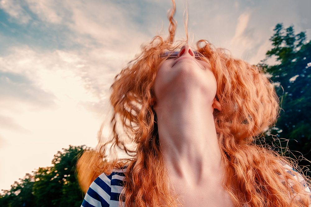 Overhappy red haired girl dancing with her face looking in the blue summer sky with clouds, copyspace on the sky. Overhappy red haired girl dancing with her face looking in the blue summer sky with clouds, copyspace