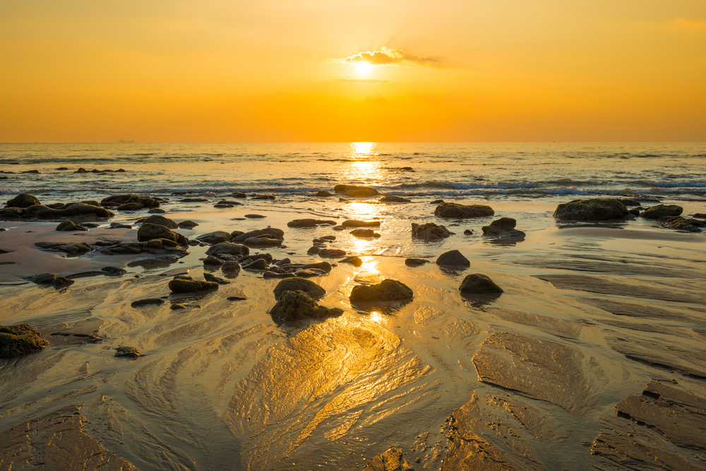 Beautiful colorful sunset landscape with sand beach, golden sun and stones at sea shore