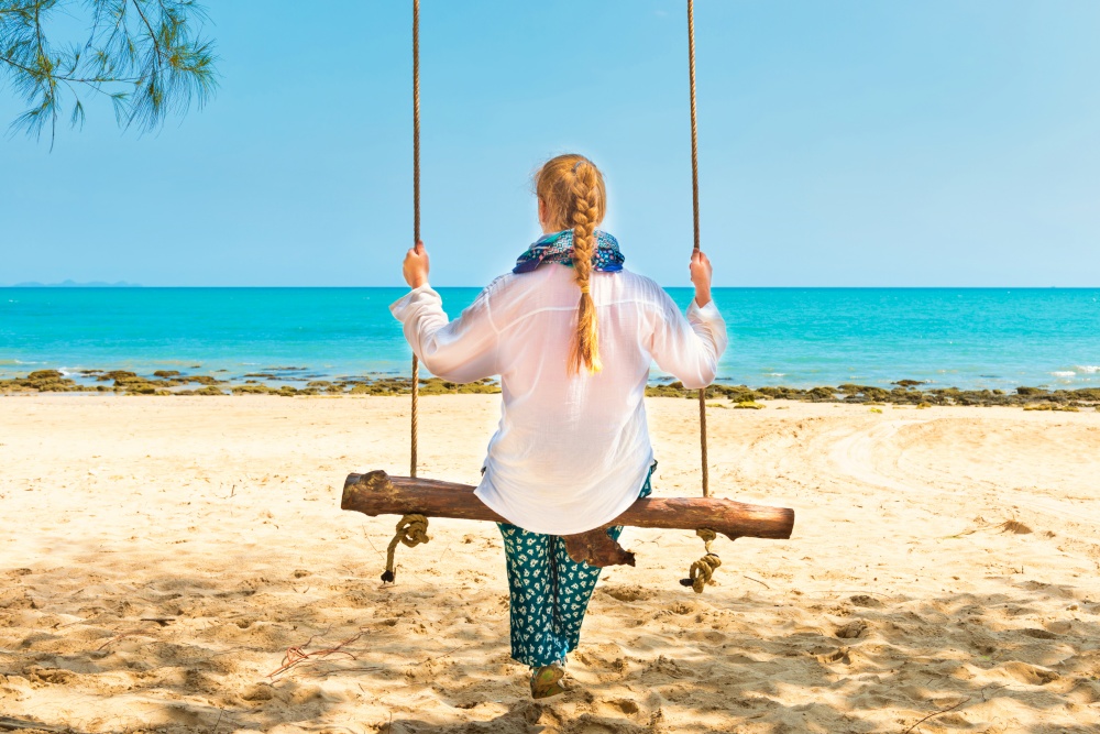 Happy pretty young woman swinging on beach swing at tropical island