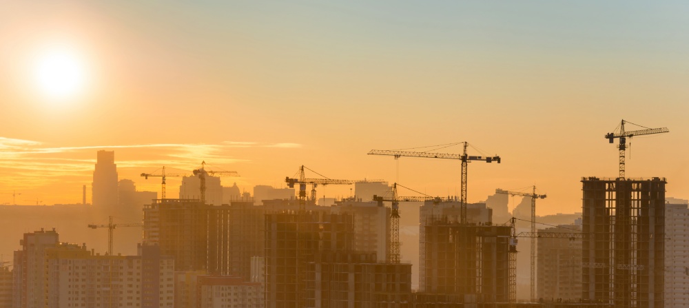 Construction site panorama with industrial cranes in city at sunset