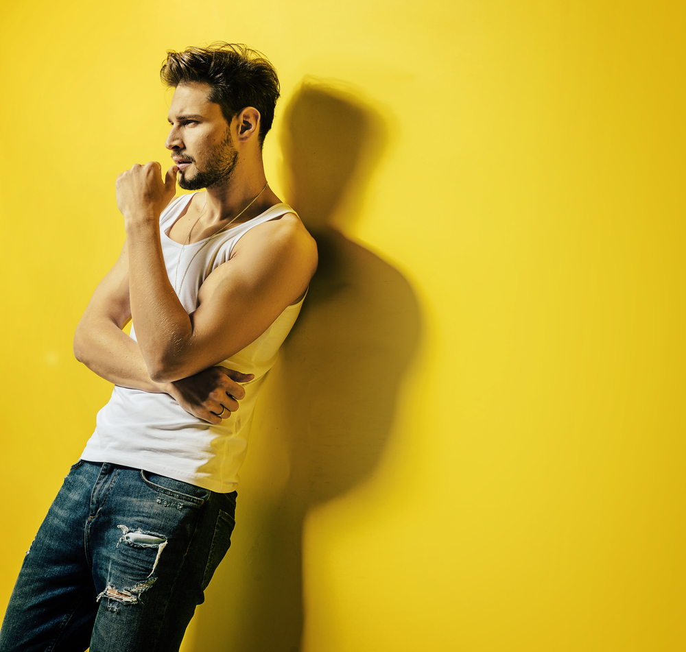 Handsome young man leaning on the bright, yellow wall