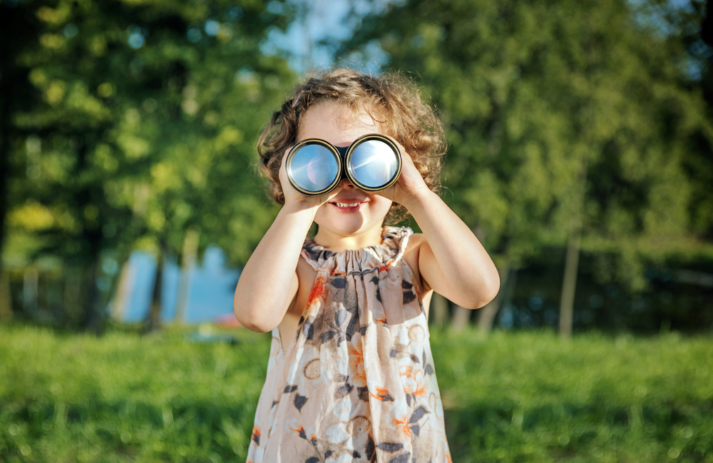 Portrait of a cheerful, little girl looking through the binoculars