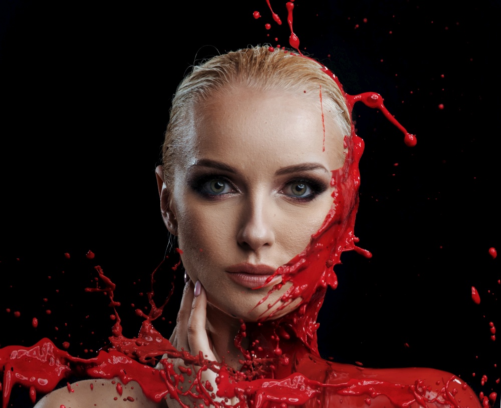 Red paint splashing against a woman&rsquo;s young face