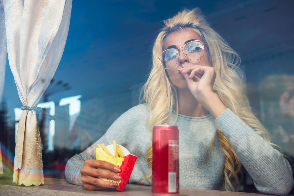 Fast food and leisure concept - beauty young blonde woman eating a fried potato in the cafe. Fast food and leisure concept