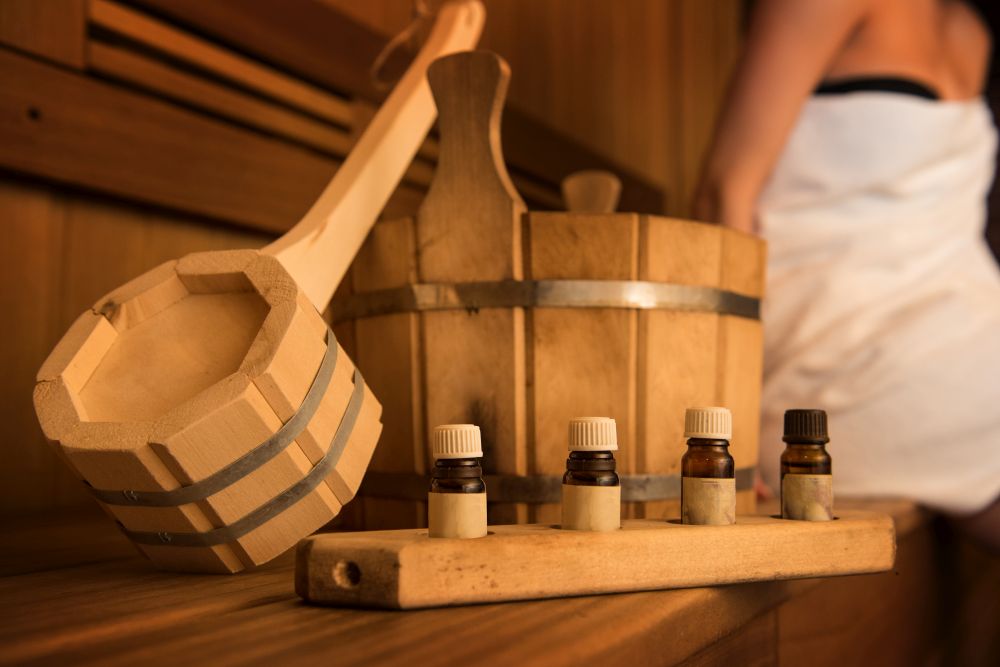 Wooden bath accessories with aromatic oil bottle for bath in the sauna and woman on background. Wooden bath accessories
