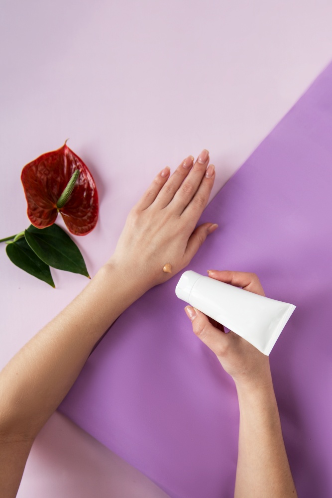 Young woman applying hand cream at color purple background. Young woman applying hand cream
