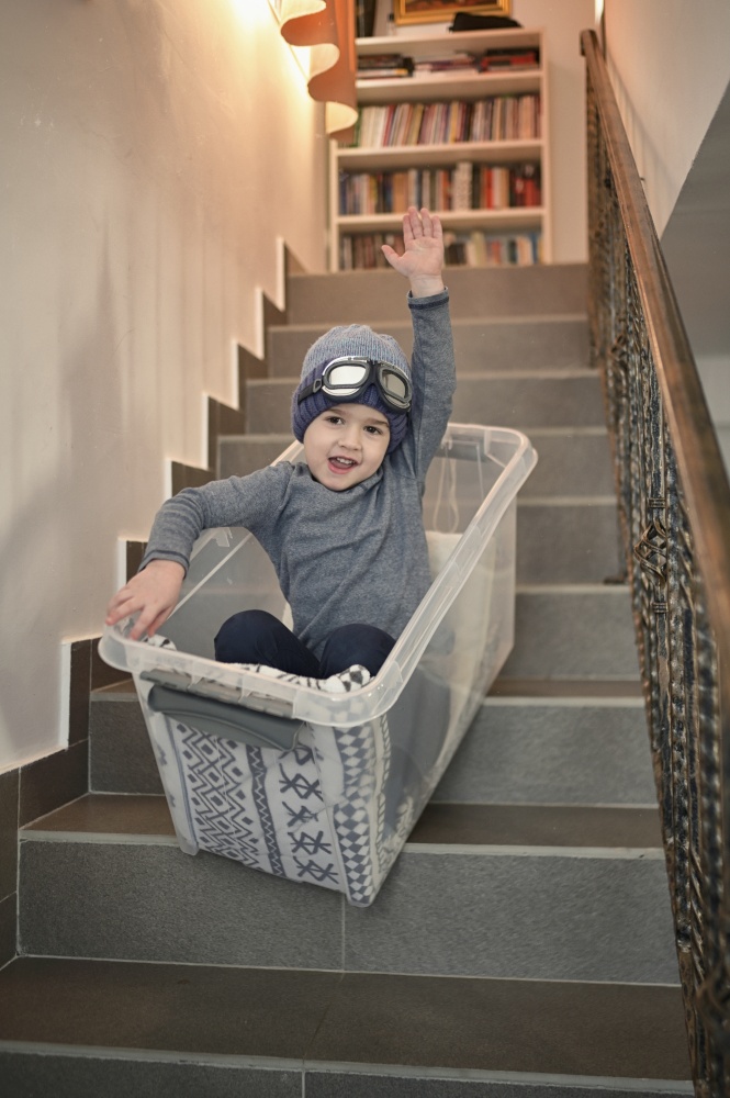 Little Boy having fun sledding down stairs in a storage box