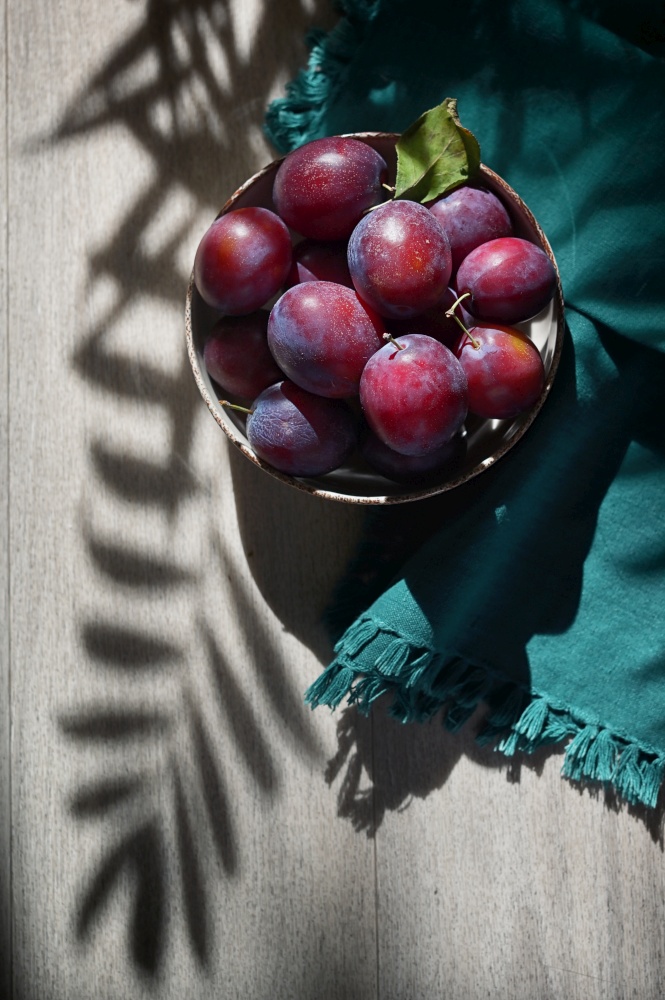 Ripe plums on Wooden Table and flower shadows
