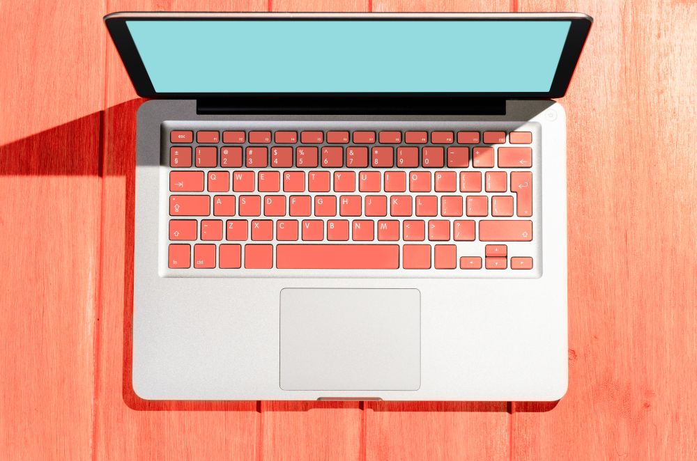 Laptop with living coral colored keyboard on wooden table on a sunny day, view from above. Laptop on wooden table