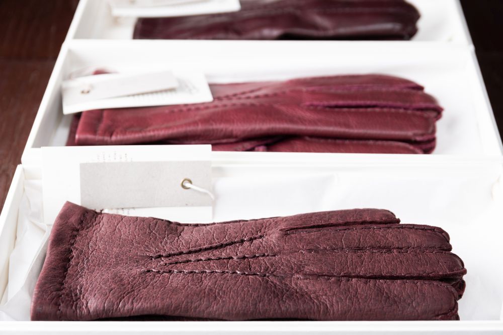 Burgundy leather gloves in boxes at luxury clothing boutique store.. men footwear boutique store