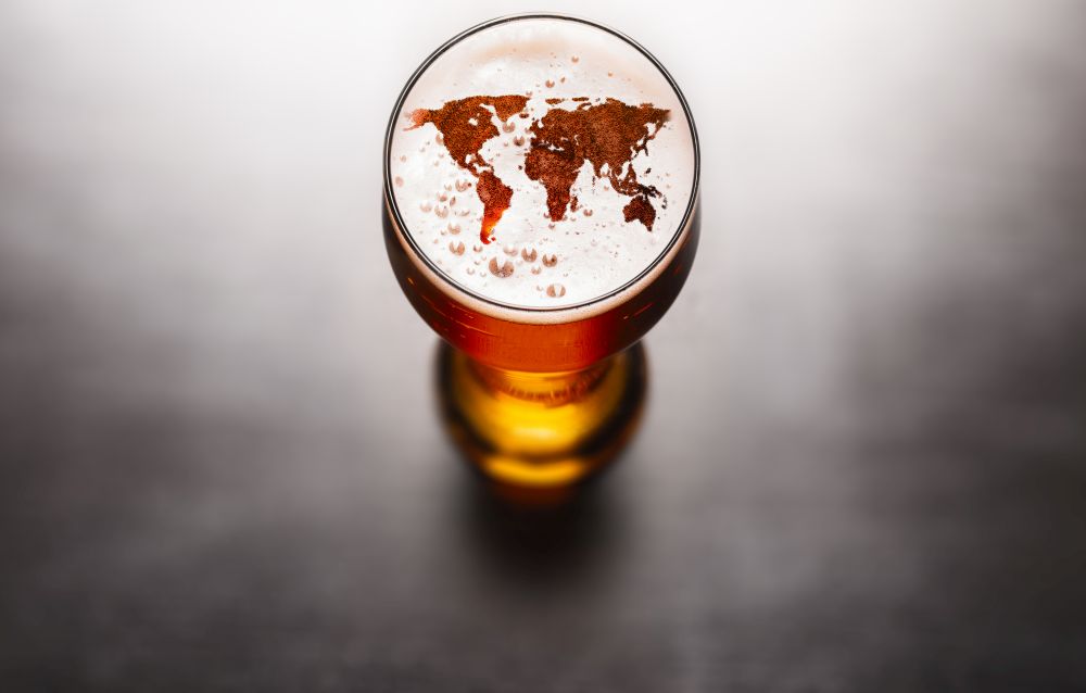 world map silhouette on foam in beer glass on black table. The continents shapes are altered ones from visibleearth.nasa.gov. lager beer on table
