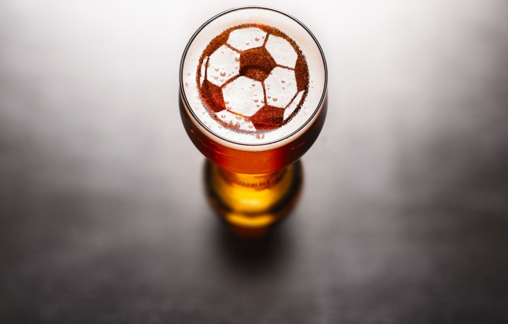 Sports bar beer concept. Soccer of football ball symbol on beer glass foam on black table, view from above. Sports bar beer concept
