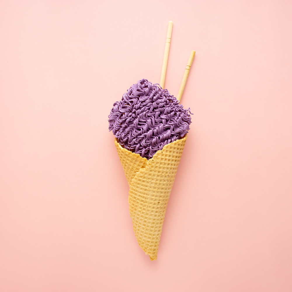 Creative food diet healthy eating concept photo of tasty painted ramen noodle pasta in waffle ice cream cone with chopsticks on white background.