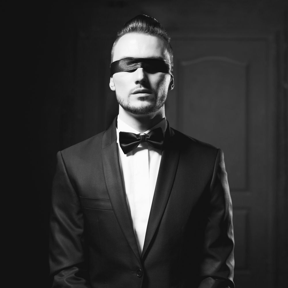 Portrait of stylish man in elegant black suit with blindfold