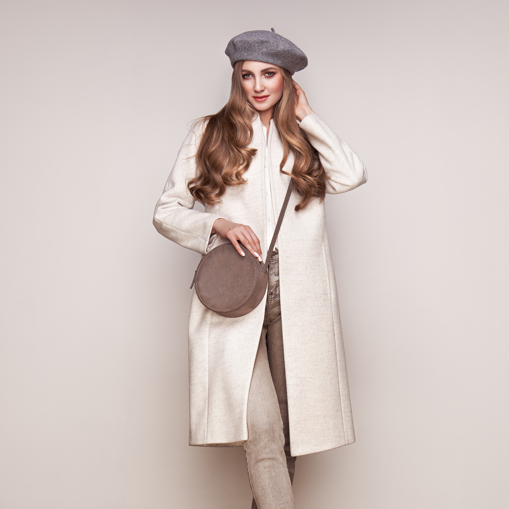 Young elegant woman in trendy white coat. Blond hair, gray beret, isolated studio shot. Fashion autumn lookbook. Model woman with handbag