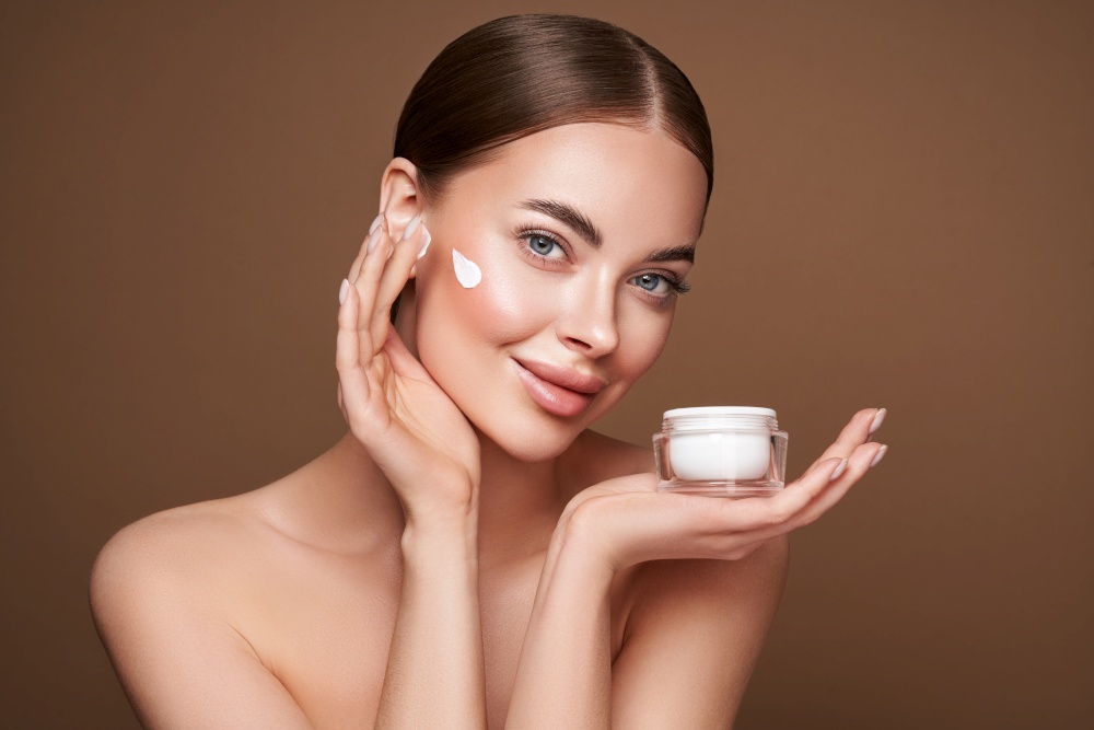 Beauty woman applying cream on her face. Young woman with clean fresh skin. Model with a jar of face cream