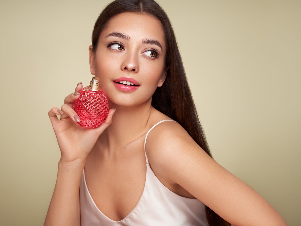 Young beautiful woman with a bottle of perfume. Model with healthy skin, close up portrait. Cosmetology, beauty and spa