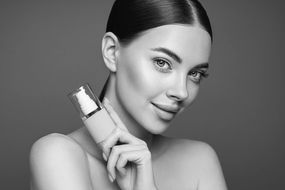 Portrait beautiful young woman with clean fresh skin. Model with foundation makeup bottle. Cosmetology, beauty and spa. Black and White photo