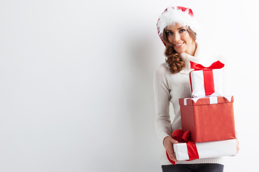 Happy woman in Santa hat with stack of Christmas gifts. Woman with stack of gifts