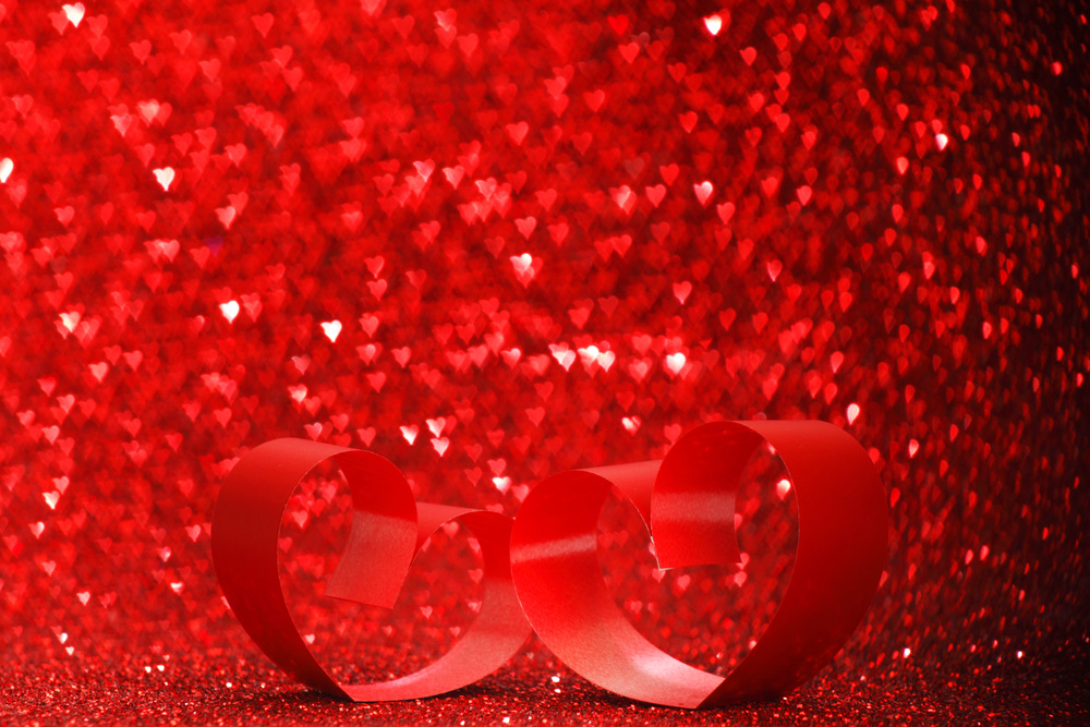 Decorative hearts of red ribbon on shiny glitter background