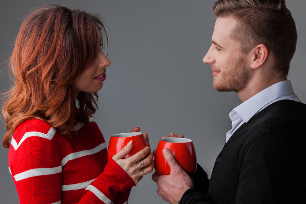 Beautiful young couple in love looking to each other holding red cups , Valentines day concept. Couple in love with cups