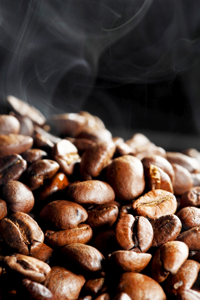 Hot roasted coffee beans and steam on black background with copy space. Hot roasted coffee beans