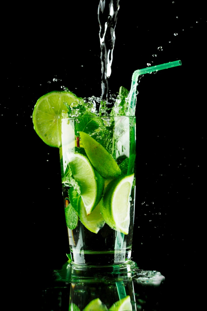Pouring fresh mojito cocktail in glass notion ice splashing isolated on black background. Pouring mojito cocktail