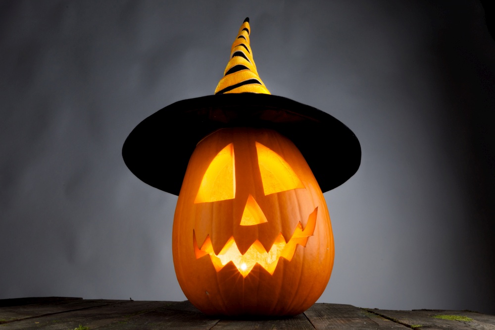 Funny Jack O Lantern Halloween pumpkin wearing witches hat on gray background. Halloween pumpkin in witches hat