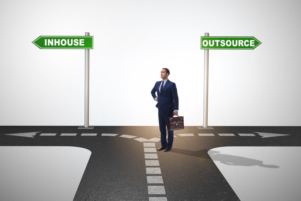 Businessman at crossroads deciding between outsourcing and inhouse . Businessman deciding between outsourcing and inhouse