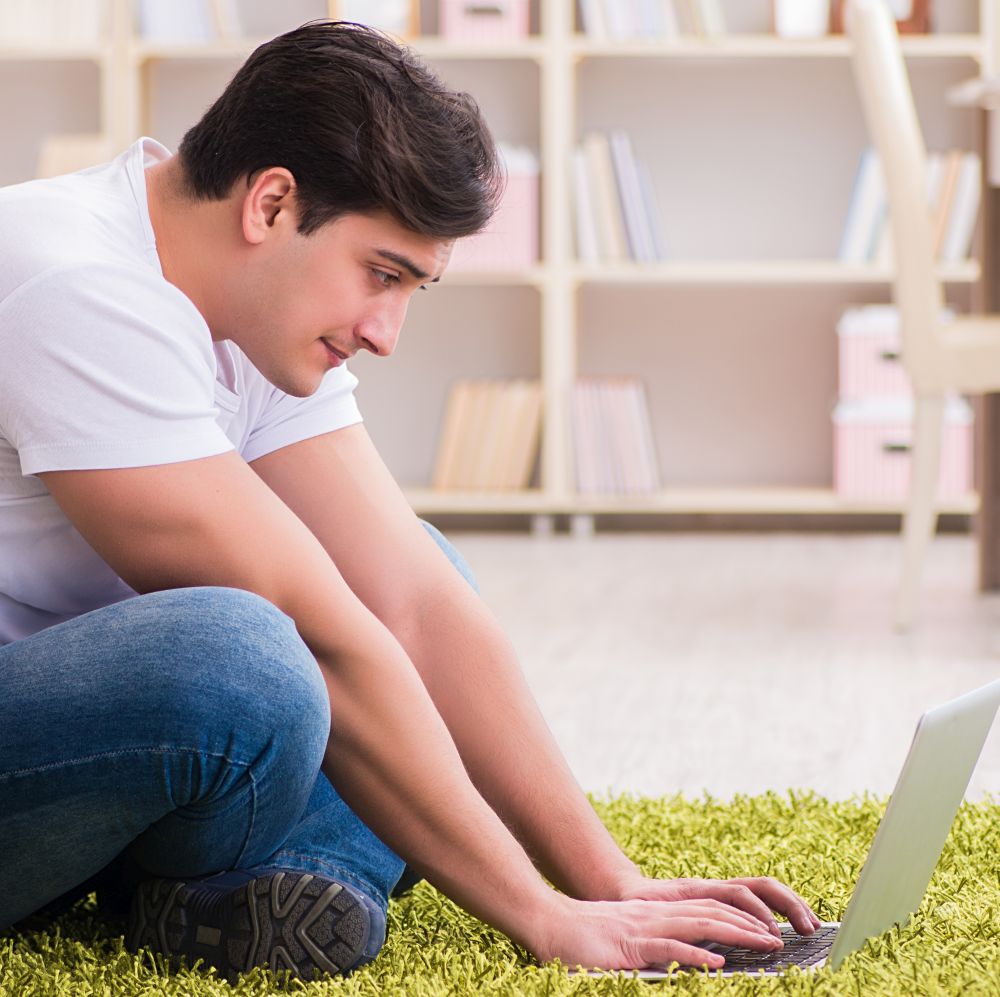 The man working on laptop at home on carpet floor. Man working on laptop at home on carpet floor