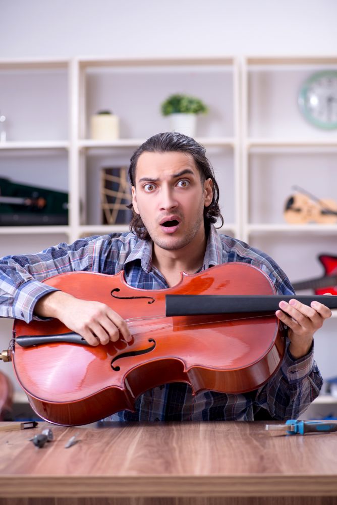 The young handsome repairman repairing cello. Young handsome repairman repairing cello