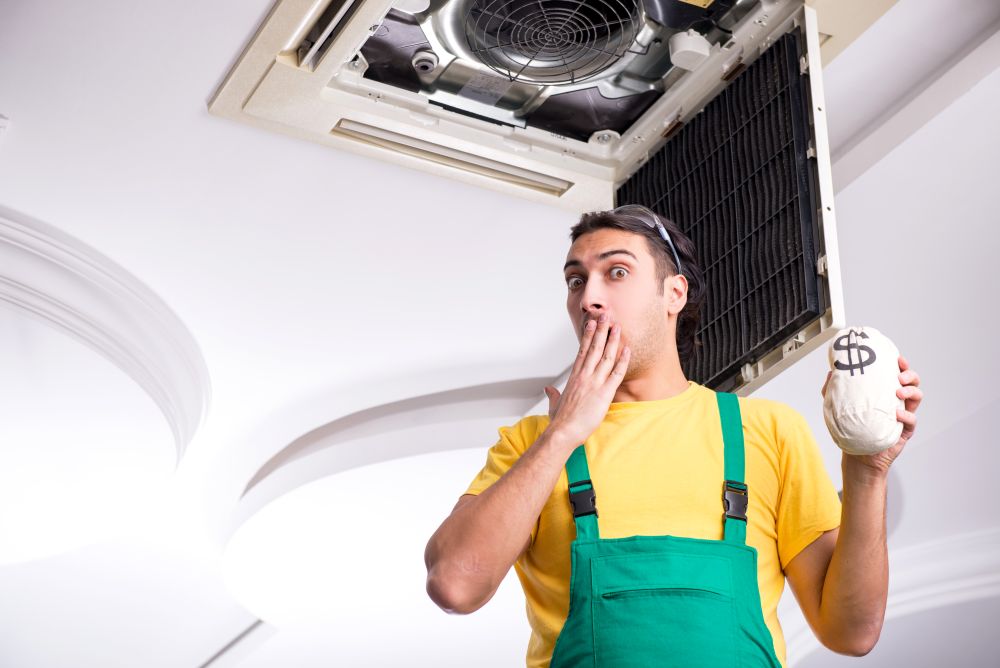 The young repairman repairing ceiling air conditioning unit . Young repairman repairing ceiling air conditioning unit