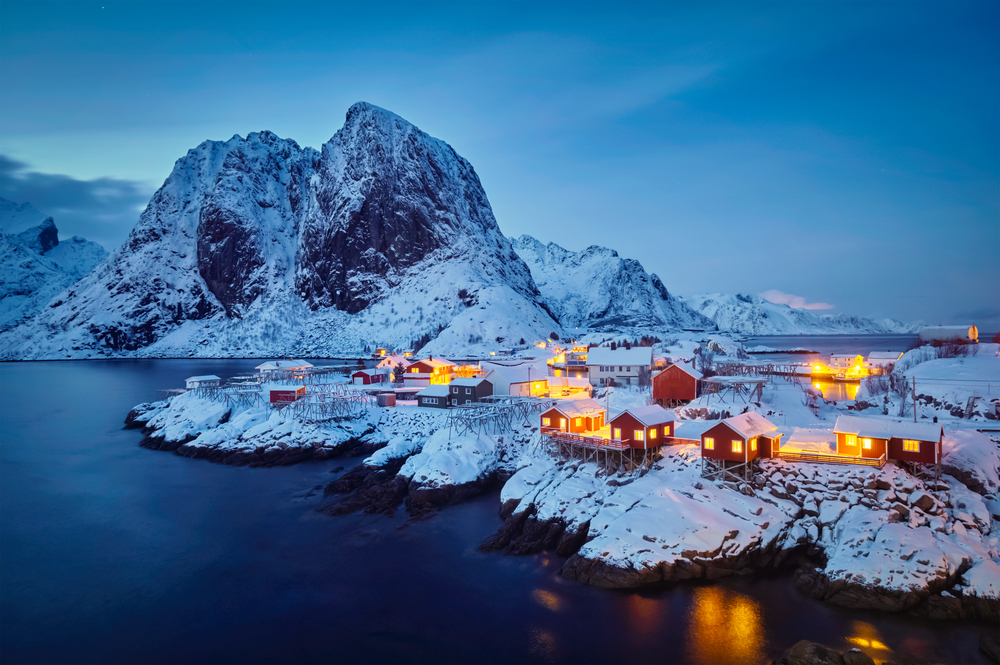 Famous tourist attraction Hamnoy fishing village on Lofoten Islands, Norway with red rorbu houses in winter snow illuminated in the evening. Hamnoy fishing village on Lofoten Islands, Norway