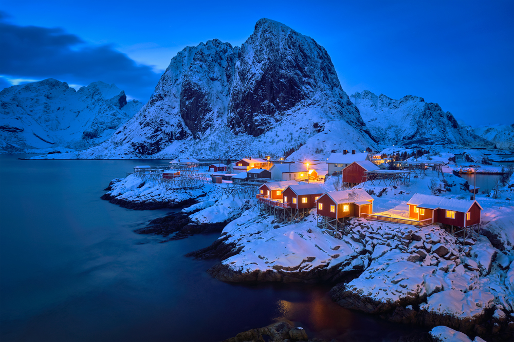 Famous tourist attraction Hamnoy fishing village on Lofoten Islands, Norway with red rorbu houses in winter snow illuminated in the evening. Hamnoy fishing village on Lofoten Islands, Norway