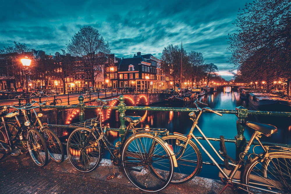Night view of Amterdam cityscape with canal, bridge with bicycles and medieval houses in the evening twilight illuminated. Amsterdam, Netherlands. Amterdam canal, bridge and medieval houses in the evening