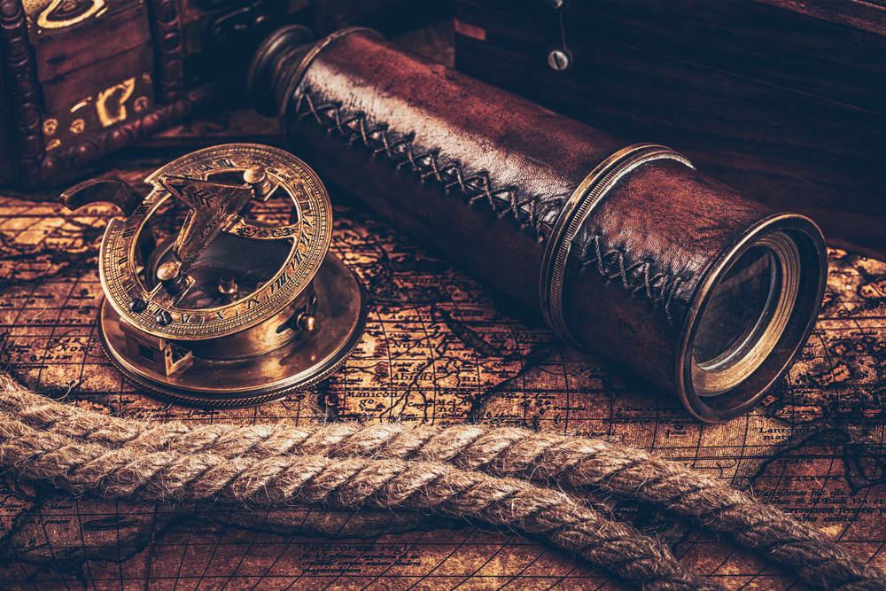 Travel geography navigation concept still life background - old vintage retro compass with sundial, spyglass and rope on ancient world map. Old vintage compass on ancient map