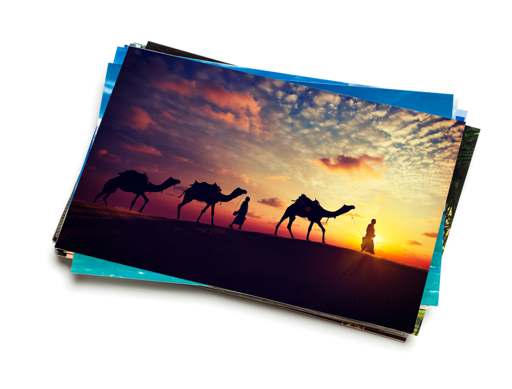 Holidays travel concept creative background - stack of vacation photos with camel caravan sunset image on top isolated on white background. Stack of vacation photos isolated