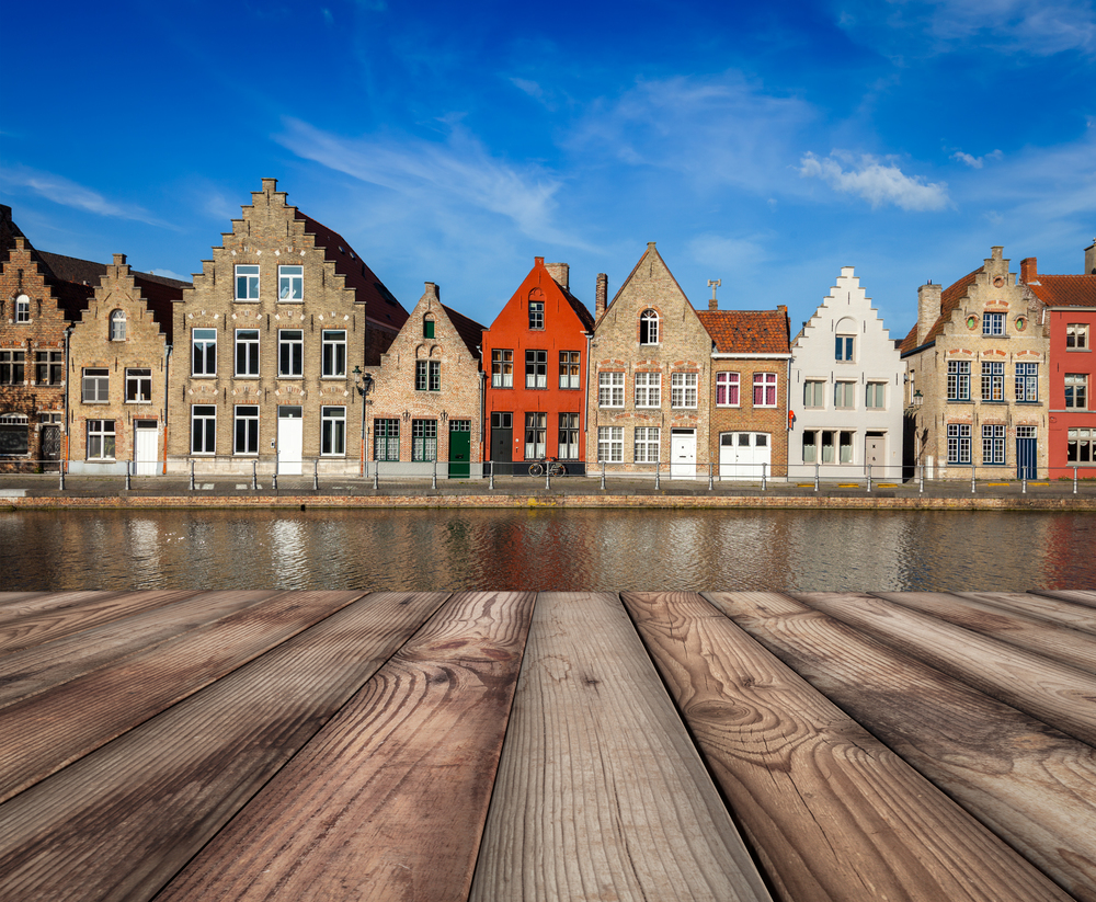 Wooden planks table with typical European Europe cityscape view -  canal and medieval houses in background. Brugge, Belgium. Wooden planks table with European town in background
