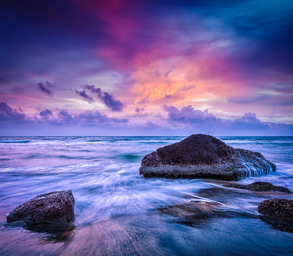 Tropical beach vacation background - waves and rocks on beach on sunset with beautiful cloudscape. Waves and rocks on beach of sunset
