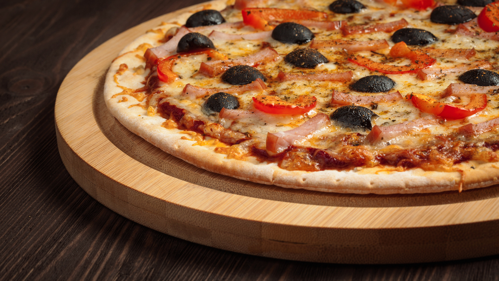 Panoramic image of ham pizza with capsicum and olives on wooden board on table close up. Ham pizza close up
