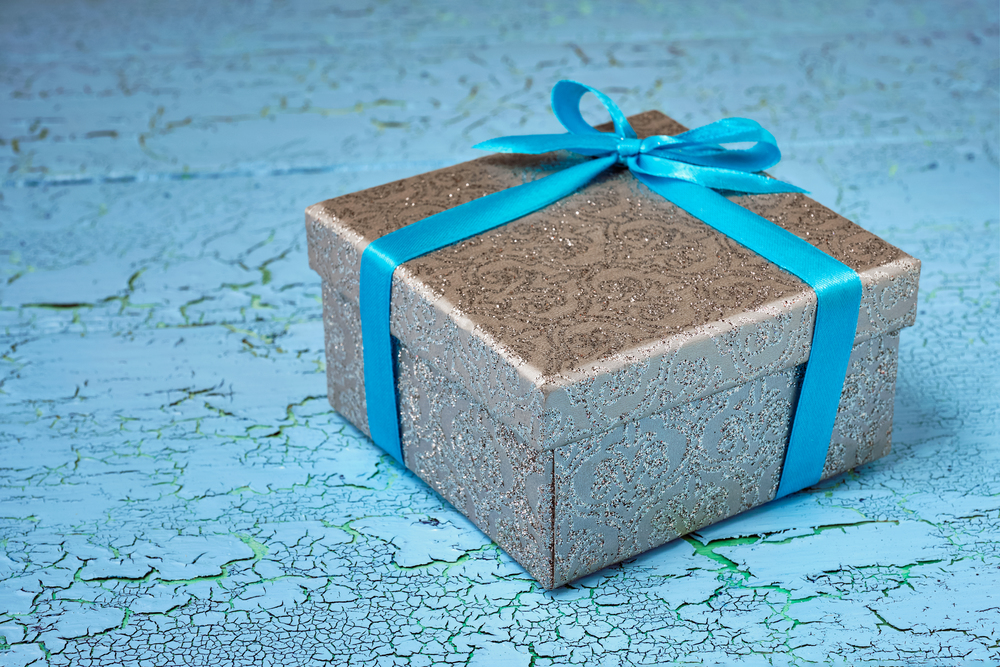 Gift birthday Christmas present concept - silver gift box with blue ribbon on blue painted wooden background. Gift box with blue ribbon