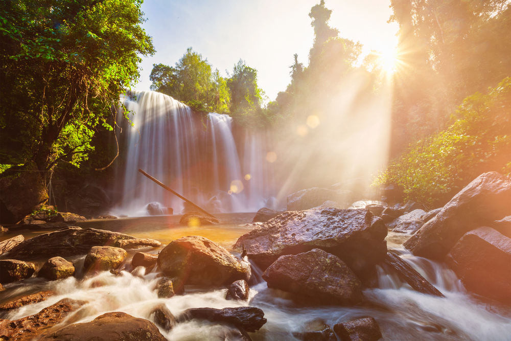 Tropical waterfall in the morning with sun rays in Cambodia. Lens flare and light leak. Tropical waterfall in the morning