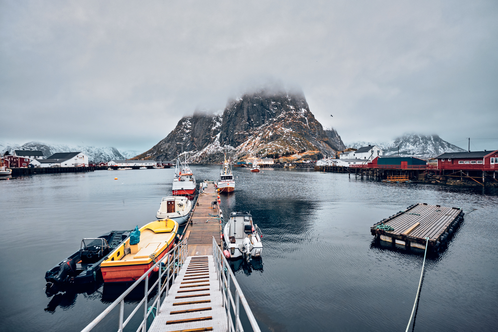 Pier with ships in Hamnoy fishing village on Lofoten Islands, Norway with red rorbu houses. With falling snow. Hamnoy fishing village on Lofoten Islands, Norway